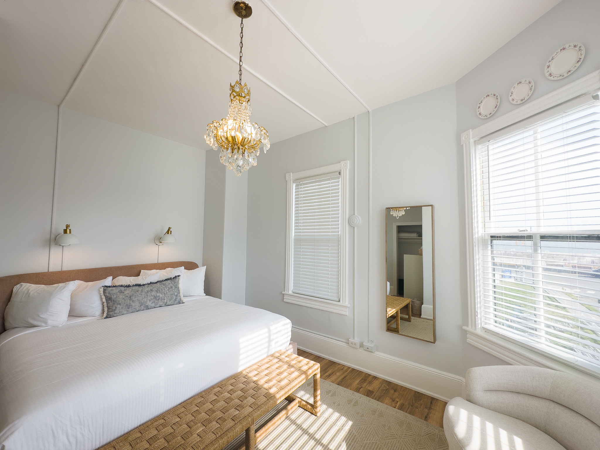 a bedroom with a bed, chair, mirror and a chandelier